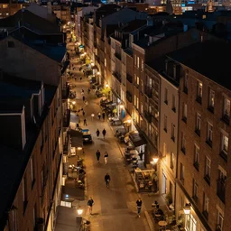 high quality photograph of a city at night, high angle photo, nightlife, people walking, 4 k professional photograph, nice place to live, midrise buildings, narrow streets, soft warm street lamps, small windows, cozy, trending on artstation, detailed, beautiful, photograph, realistic
