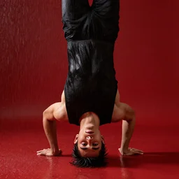 Wet young man suffers standing on his head in the red room rain