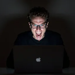 an award - winning editorial medium shot studio photographic portrait of a white man with short curly hair glasses behind his laptop. he is yelling in anguish. the glow of the laptop screen is lighting his face from below. mood is choatic and omnimous with very dramatic lighting. in the style of annie leibovitz