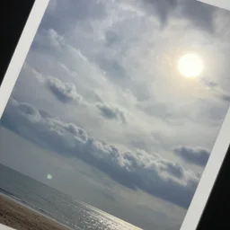 a photo, on top of the photo a cloudy sky visible, at right corner of photo we see the sun, left corner is sea and beach