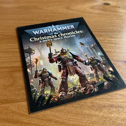 postcard showing 'warhammer the christmas chronicles: a merry space marine' laying on coffee table, zoomed out, HD, iphone capture