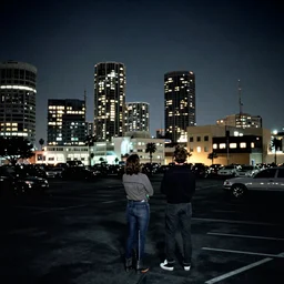 looking up at a sprawling building complex seen from a dark parking lot in los angeles at night. 1 9 9 0 photo by james cameron