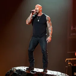 dwayne jonson singing in a rock concert standing on a rock