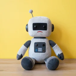 a plush toy robot sitting against a yellow wall