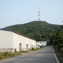 a road next to warehouses, and a hill behind it with a radio tower on top