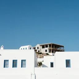 Minimalistic background of buildings with traditional Greek style architecture. Low angle view of white houses against a blue clear summer sky. Construction of a modern residential building in the open air.