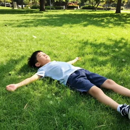 A photograph of a boy laying on the grass in a park on a sunny summer day