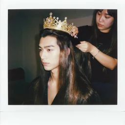 handsome man with shiny and silky long hair getting hair styled by a hair queen wearing a golden crown studded with diamonds, polaroid