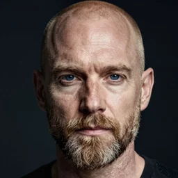 photograph of a balding, bearded middle aged blond man, with dark blue eyes, and very pale skin