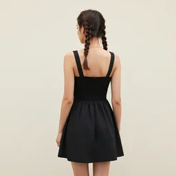 a girl with plaits, wearing a black summerdress, back view, in front of a stucco wall