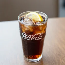 a cup of coca - cola with ice cubes ， lemon pice ， on a table