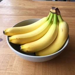 a photograph of a bowl of bananas sitting on a wooden table, taken on iphone 1 3, natural lighting