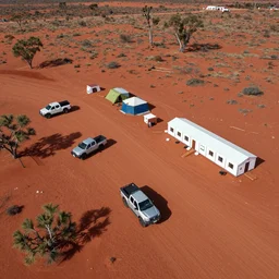 aerial drone photograph of a campsite on the border of the australian red desert with pickup trucks, tents and prefab medical center