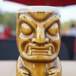 a closeup photorealistic photograph of a glossy ferrari themed tiki mug at at an outdoor trader vic's bar featuring the happy enzo ferrari's face. tiki theme. bright scene. fine detail. this 4 k hd image is trending on artstation, featured on behance, well - rendered, extra crisp, features intricate detail, epic composition and the style of unreal engine.