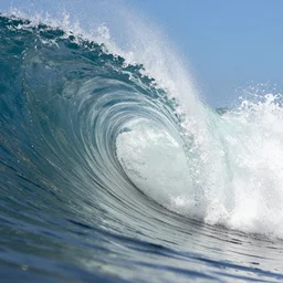 high - speed extreme close - up photography through the perfect curl of a breaking ocean wave catching the sunlight, water spray, blue sky