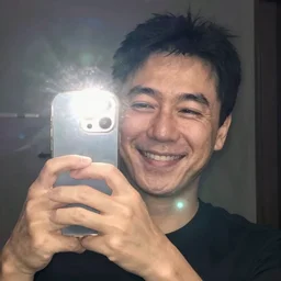 my Japenese dad accidentally taking a selfie with the front camera, smiling, squinting his eyes because the camera flash is so bright in his face