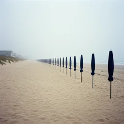 rows of open beach umbrellas lining a sandy cape cod beach, fog, contemporary archival color photograph print from the original negative, by stanley kubrick
