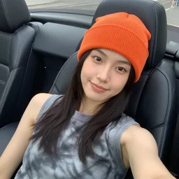 girl lounging in the leather seats of a convertible car wearing an orange beanie and a grey tie-dye sleeveless shirt, selfie, faint smile