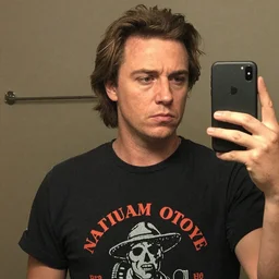 napoleon dynamite with a blank expression while wearing a graphic t - shirt and taking a selfie, grainy quality, low quality, low resolution, realistic, hyperrealistic, very realistic, hd quality, intricate details, very detailed, grainy, taken on an iphone