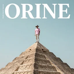 Magazine style cover photo of a pastel colored men wearing a gray hat on top of his head. Standing on top of a pyramid. wide angle lens, f2/8