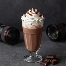 food photography of hot chocolate drink in tall glass with cream on top and cocoa powder, chocolate pieces, canon macro lens, moody lighting, stock images, front angle view