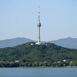 a hill with a radio tower next to a lake, hills in background. telephoto lens photography.