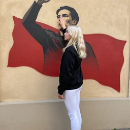 platinum - blonde - haired hime - cut blue - eyed 1 9 - year - old nordic princess wearing white leggings and black jacket, adoring communist mural on wall, post - revolutionary era, toulouse france