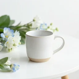 clay mug on a white table surrounded by elegant blue and white flowers and green leaves, bright white realistic, up close shot, white background, zen, light, modern minimalist, clean f 2 0