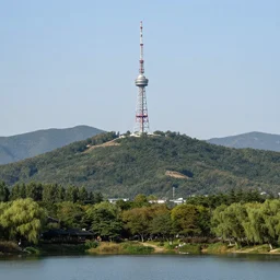 a hill with a radio tower next to a pond, hills in background. telephoto lens photography.