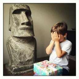 a kid looking very dissapointed that his birthday present was a very large moai statue | iphone photograph