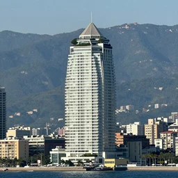 skyscraper with forset on the roof and balconies, located on the seashore, mountains can be seen behind