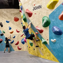 “4k realistic dlr photograph of an indoor rock climbing wall, colorful mural on the wall says JOHN”