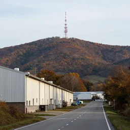 a road next to warehouses, and a autumn hill background with a radio tower on top, 3 0 0 mm telephoto lens