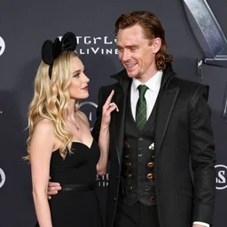 Tom Hiddleston dressed as his character Loki and flirting with a skinny blonde woman wearing Mickey Mouse ears