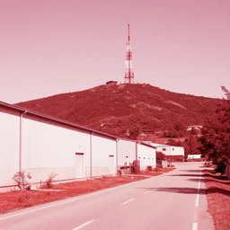 a road next to warehouses, and a hill behind it with a radio tower on top, 9 0's camera filter, red tint