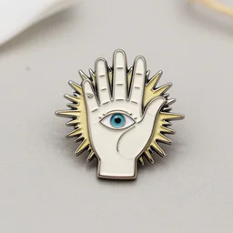a photograph of an enamel pin depicting a hand with an eye in it, sunburst surrounding the hand, etsy product photo
