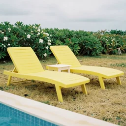 two yellow beach beds next to a pool, yellowish grass, green bushes in the background with white flowers, grainy photograph, diagonal composition, cloudy day, focus on the beach beds