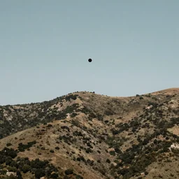 a black dot in the sky above a hilly mountain, landscape