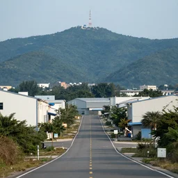 looking down road, warehouses lining the road. hills background with radio tower on top. telephoto lens compression.