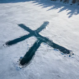 photo of a lake covered in snow. the snow has melted in a cross shape and blue water can be seen. arial picture