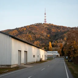 a road next to warehouses, and a hill background with a radio tower on top, autumn