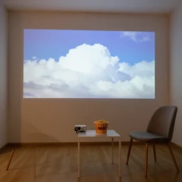 a room with with a projector projection a video of clouds, a single chair and small table with a bucket of popcorn is on the table
