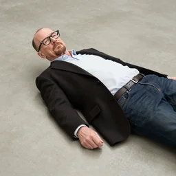 walter white with a black reading glasses while laying on a smooth concrete floor