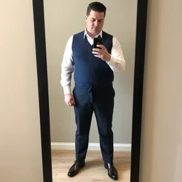 clean - shaven portly white man with neatly styled black hair in his 4 s is wearing a dress shirt sweater - vest trouser dress shoes. his is standing in front of a mirror, taking a photo of himself.