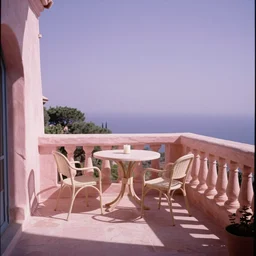 a high definition film photograph pov holiday balcony. pastel pink stone, lavender sky, table, chairs, candle.
