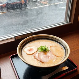 A top view of a tonkotsu ramen next to a window on a rainy day
