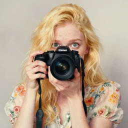 pale young woman with bright blonde hair, freckles, big bright eyes and a very wide face, flowery dress, she is holding a professional dslr camera close to her face with her hands, expressive, surrealism, emotional watercolor art by conrad roset