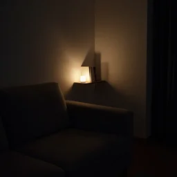 a room in darkness with a couch and a small shelf with book lit by a dim light.