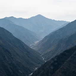 A photo where the mountains are towering over the valley below their peaks shrouded in mist. The sun is just peeking over the horizon and the sky is ablaze with colors. The river is winding its way through the valley and the trees are starting to turn yellow and red.