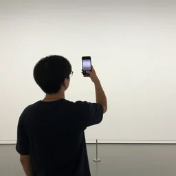 person seen from behind standing in an empty gallery contemplating over the empty opposite wall smartphone screen in hand overhead, photo taken with provia